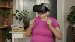 En äldre dam sitter framför ett fönster med VR-glasögon på sig.